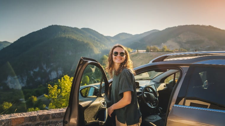 Young woman standing outside car overlooking a mountainside.