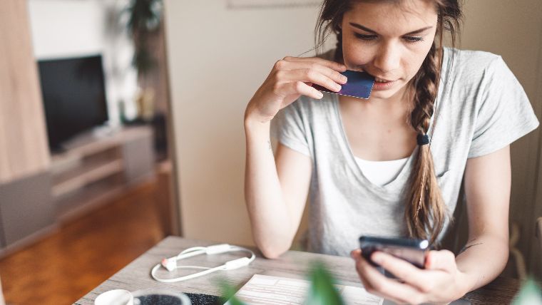Nervous woman biting credit card while looking at phone.