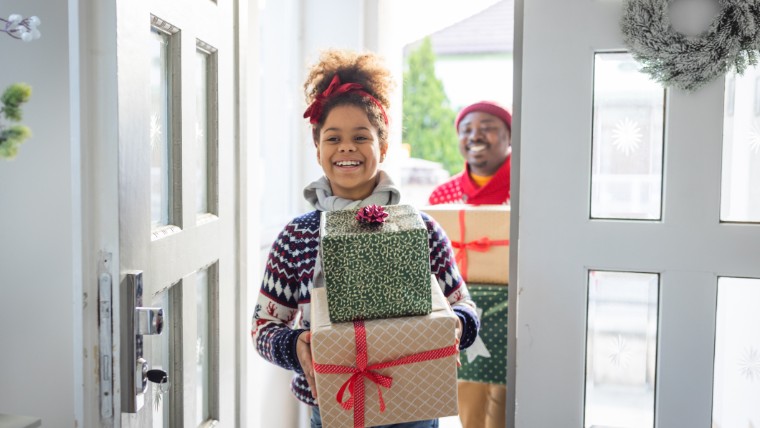 Young girl walking through door with wrapped presents.