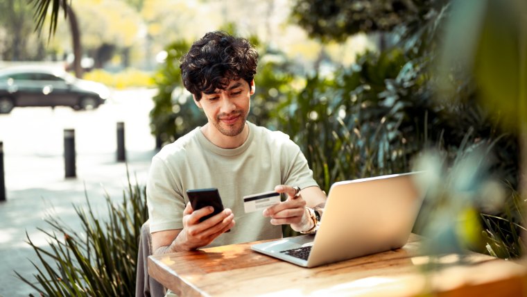 Young man sitting at cafe making credit card payment on phone.