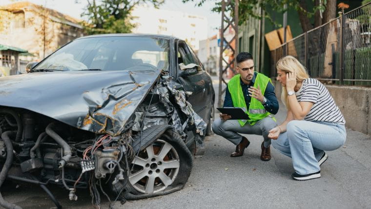 Driver and insurance adjuster looking at wrecked car.