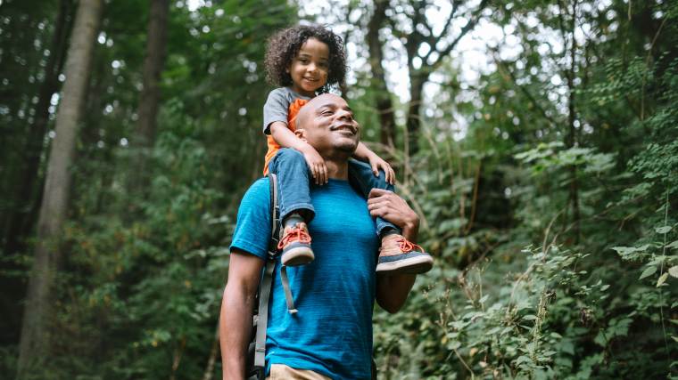 Man enjoying nature while carrying his young daughter on his shoulders.