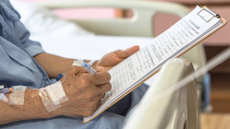 The hands of an elderly patient in a hospital as they sign paperwork.