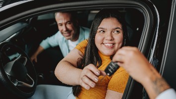 Young woman sitting in car being handed the keys.