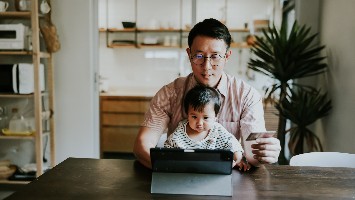 Young father with baby on lap making online purchase while holding credit card.
