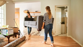 Two women carrying couch out of apartment.
