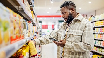 Man checking phone while browsing shelves at store.