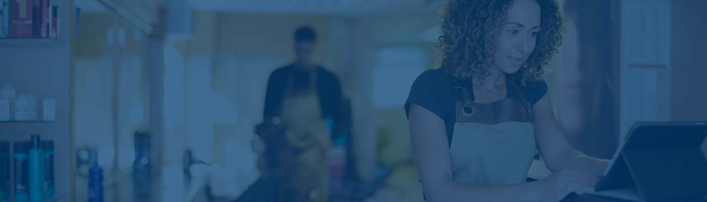 Banner image of a small business owner at a salon working on a tablet.