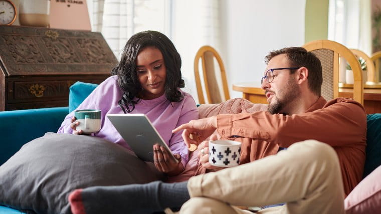 Couple sitting on couch and looking at tablet together.