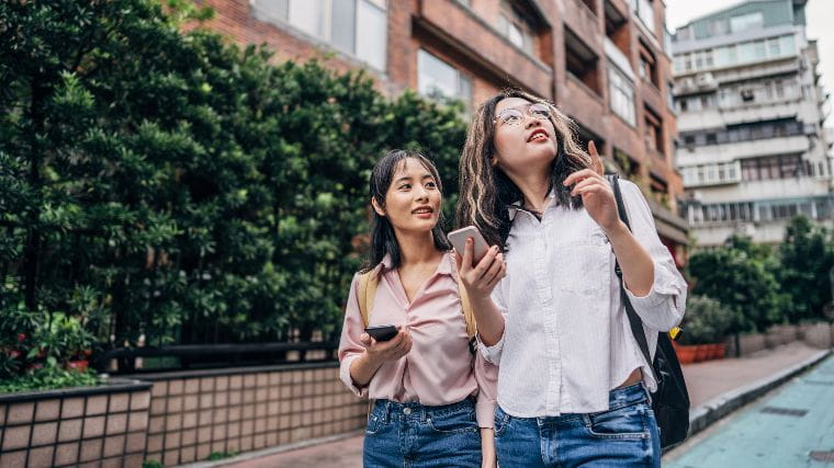 Two young women walking down street while looking for an apartment.