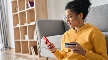Young woman using smartphone and making purchase with credit card.