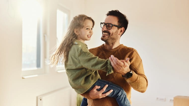 Father holds young daughter in his arms.