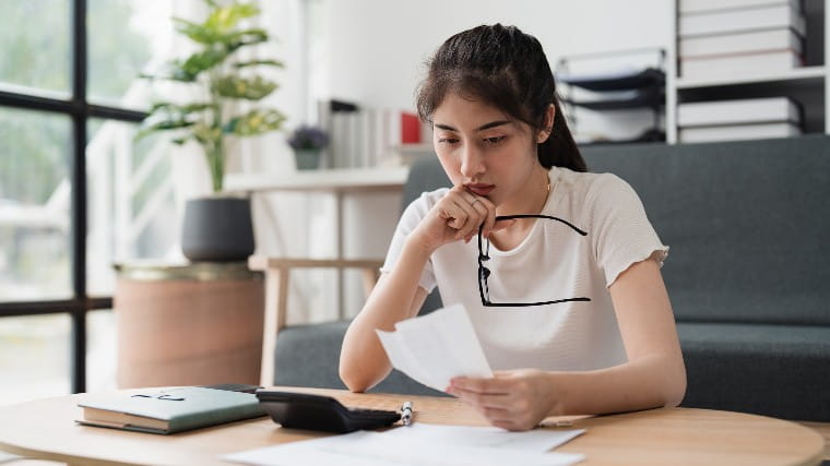 Young woman holding glasses and reading piece of paper.