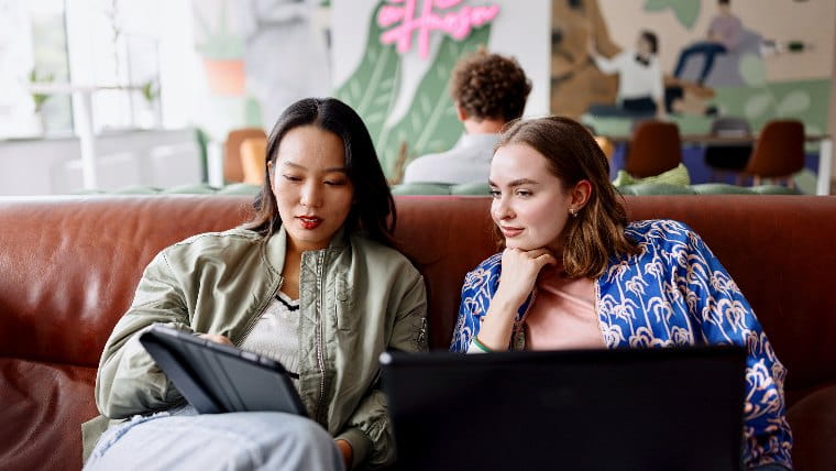 Two young women comparing information on a tablet.