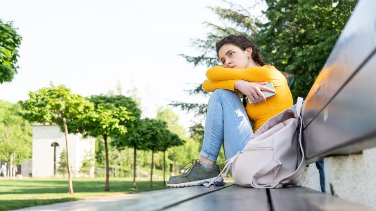 Sad young woman sitting on a bench in a park.