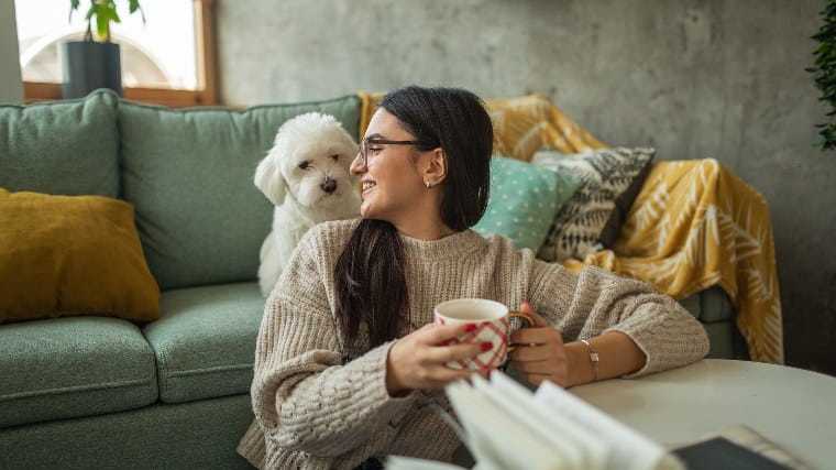 Young woman drinking tea with small dog in apartment.