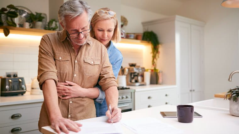 Senior couple in kitchen reviewing paperwork.