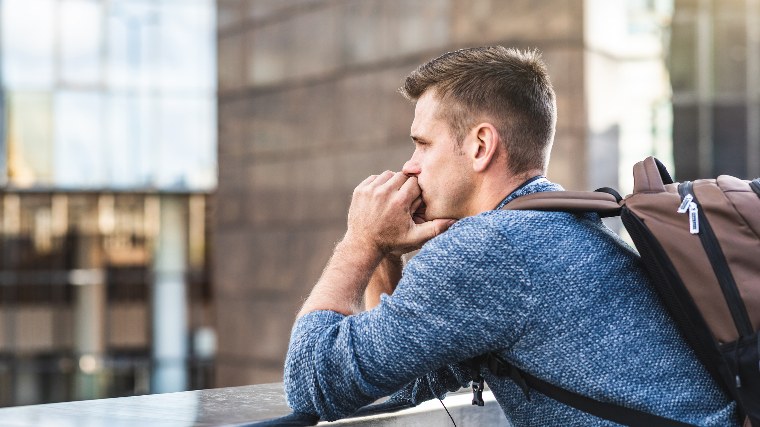 Man with backpack standing on bridge looking thoughtful.