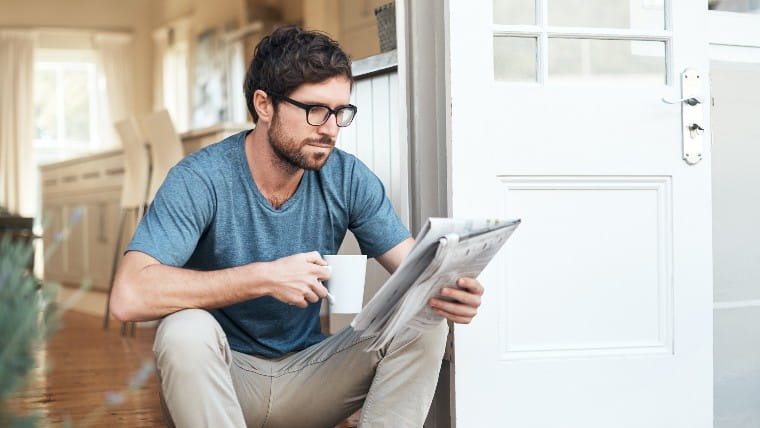 Man reading newspaper and drinking coffee.