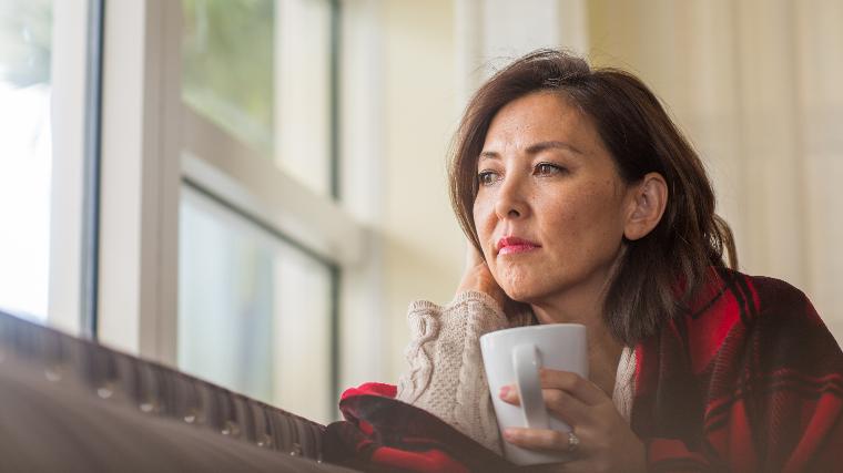 Woman wrapped in blanket looks out the window.