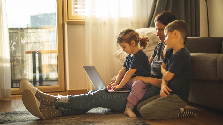 Mother sits with two children on floor of apartment.