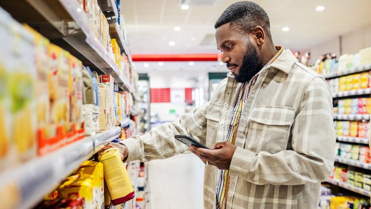 Man checking phone while browsing shelves at store.