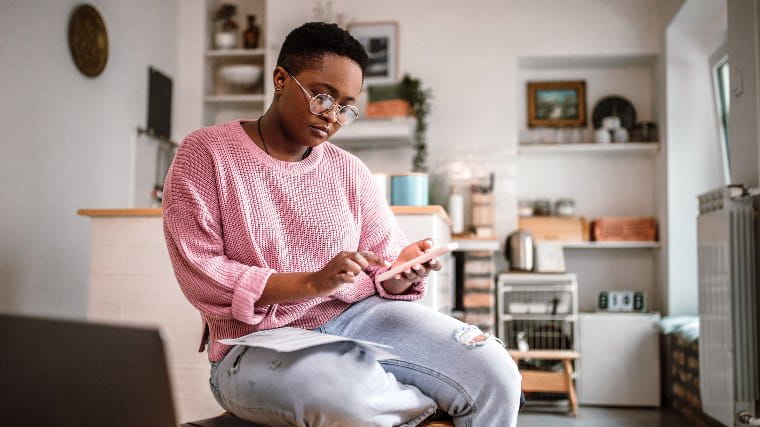 Young woman using smartphone while filling out paperwork.