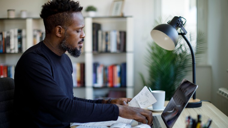 Man using laptop while reading bills.