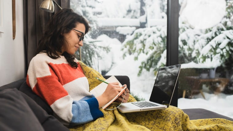 Young woman working on laptop with winter scene in background.