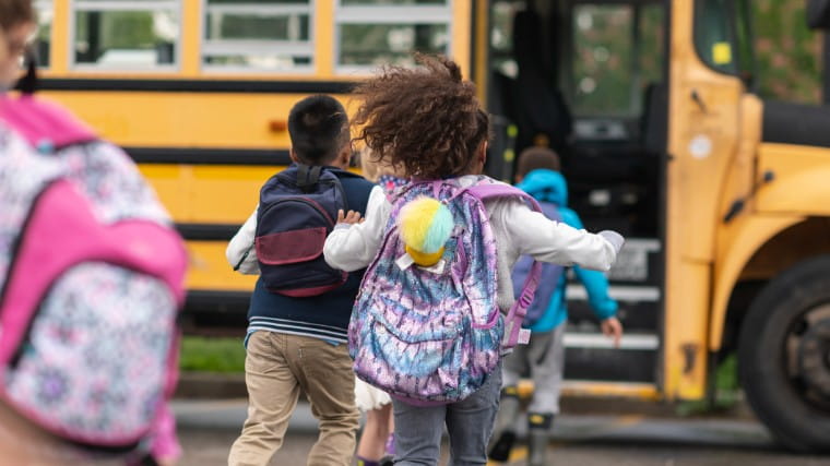 Young children with backpacks running to school bus.
