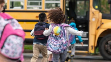 Young children with backpacks running to school bus.