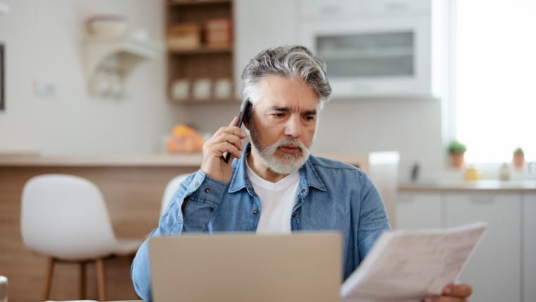 Older man talking on phone while reading bill.