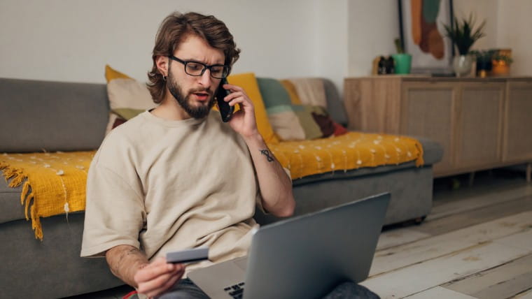 Concerned man looking at credit card while talking on phone.