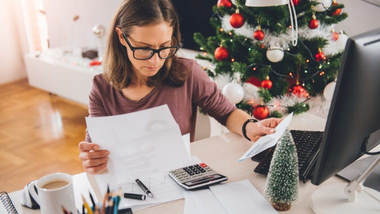 Woman reviewing bills in front of holiday decorations.