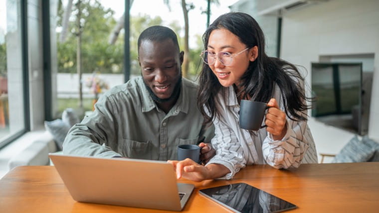 Two young adults drinking coffee and looking at laptop.