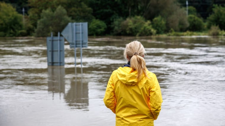 Woman in rain jacket looking at flood water.