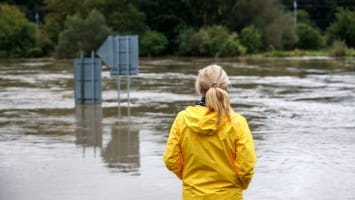 Woman in rain jacket looking at flood water.