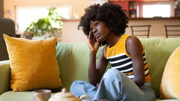 Young woman sitting on couch looking stressed out.