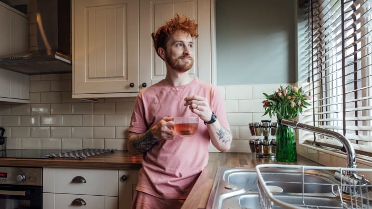 Young man enjoying cup of tea in his kitchen.