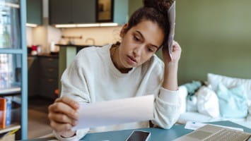 Stressed out young woman reading utility bill.