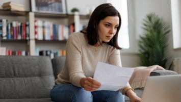 Worried young woman holding a bill.