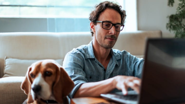 Man uses laptop while sitting next to beagle.