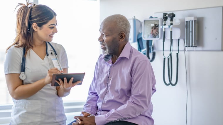 Senior man in hospital speaking with nurse.