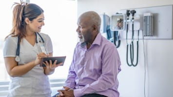 Senior man in hospital speaking with nurse.