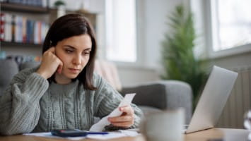 Worried young woman looking at bills.