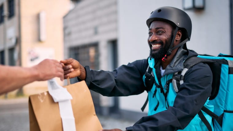 Delivery man hands paper bag to customer.