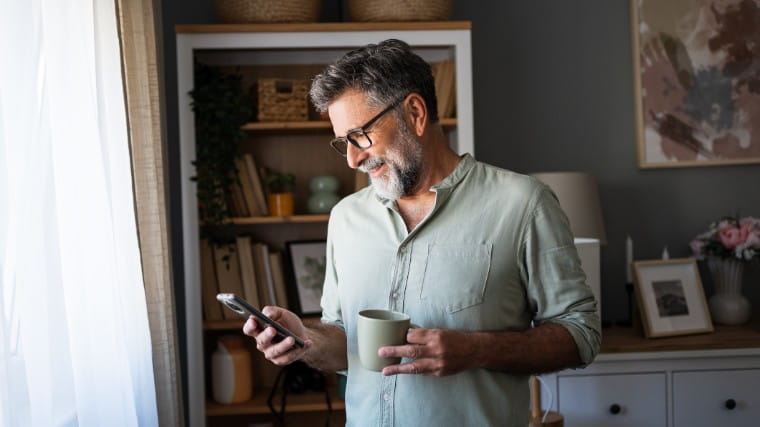 Man holding coffee cup while using cellphone.