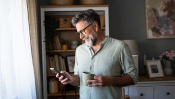 Man holding coffee cup while using cellphone.