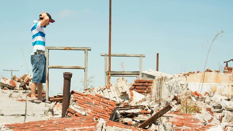 man looking at ruins of home after a disaster