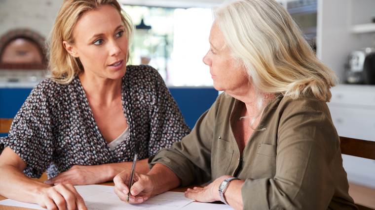 woman assisting older woman as she signs documents